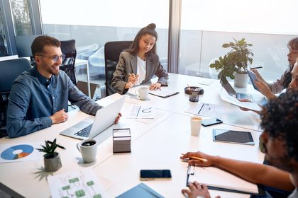 A diverse team of professionals engaged in a meeting, with check in question, with laptops and notepads, discussing ideas and collaborating on projects.