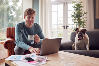 Man holding a cup of coffee, a laptop on his table, and working from home.